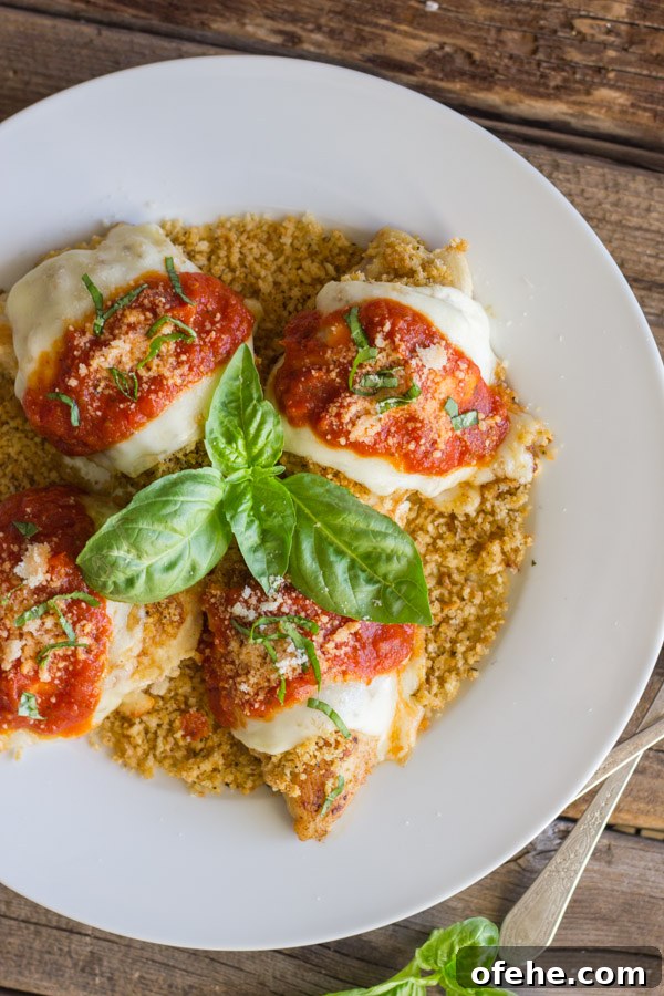 Easy Chicken Parmesan With Toasted Panko on top of a thin layer of the toasted Panko on a serving plate, topped with red sauce, grated Parmesan and some thinly sliced fresh basil, with fresh basil leaves in the center of the serving plate.  