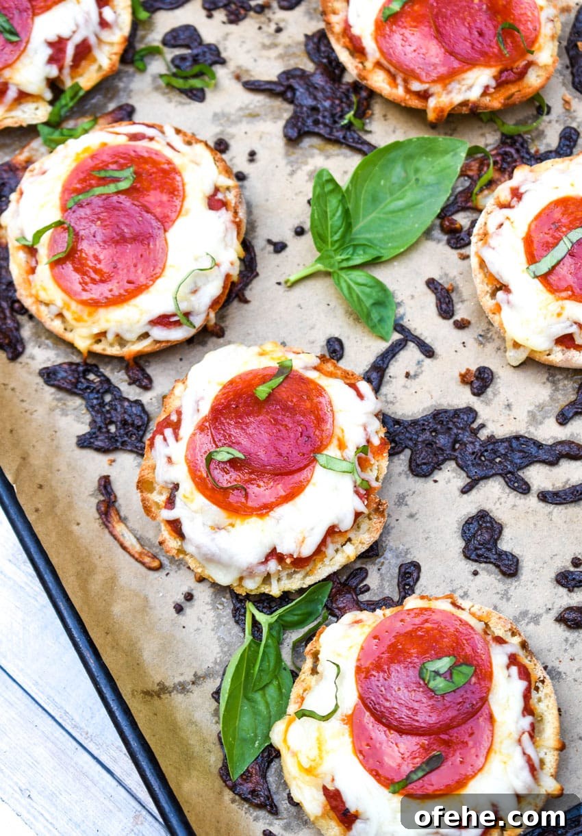 Mini English Muffin Pizzas: Quick Homemade Lunch or Snack 3 english muffin pizzas on a parchment paper lined baking sheet
