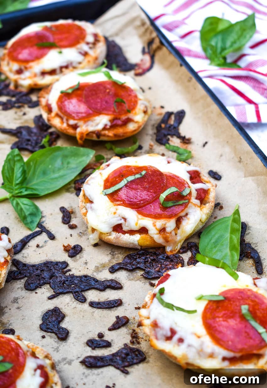 Mini English Muffin Pizzas: Quick Homemade Lunch or Snack 4 english muffin pizzas on a parchment paper lined baking sheet