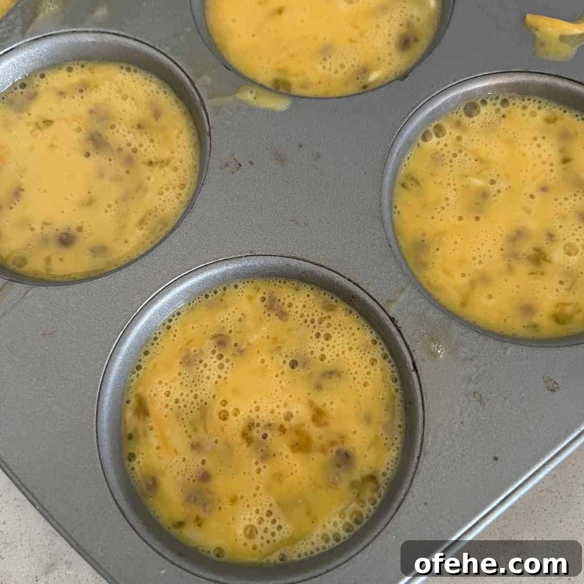 Carnivore Egg Bites Recipe with Bacon and Cheese 5 Egg mixture in a mini muffin pan.