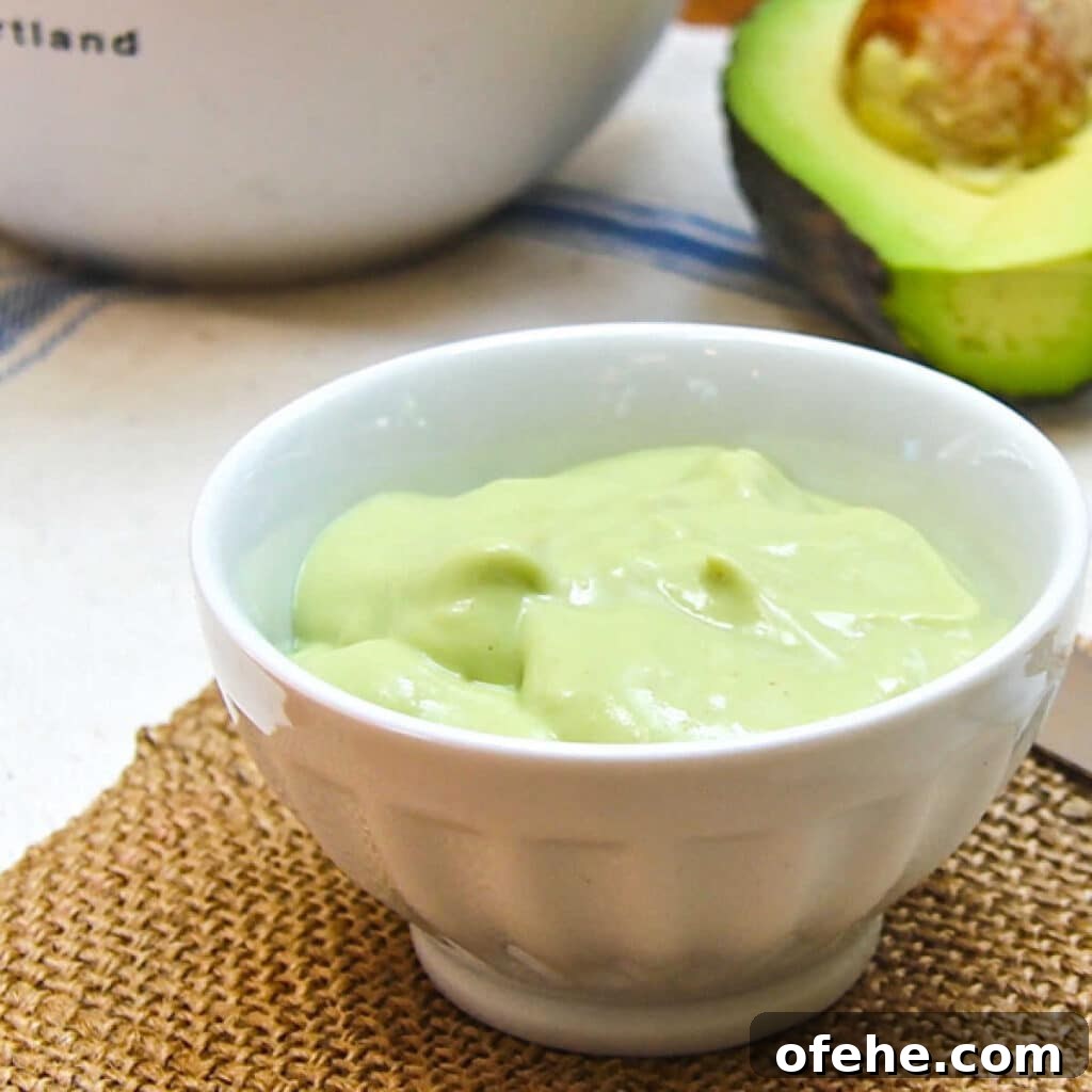 Small bowl of avocado cream, with a cut avocado in the background.