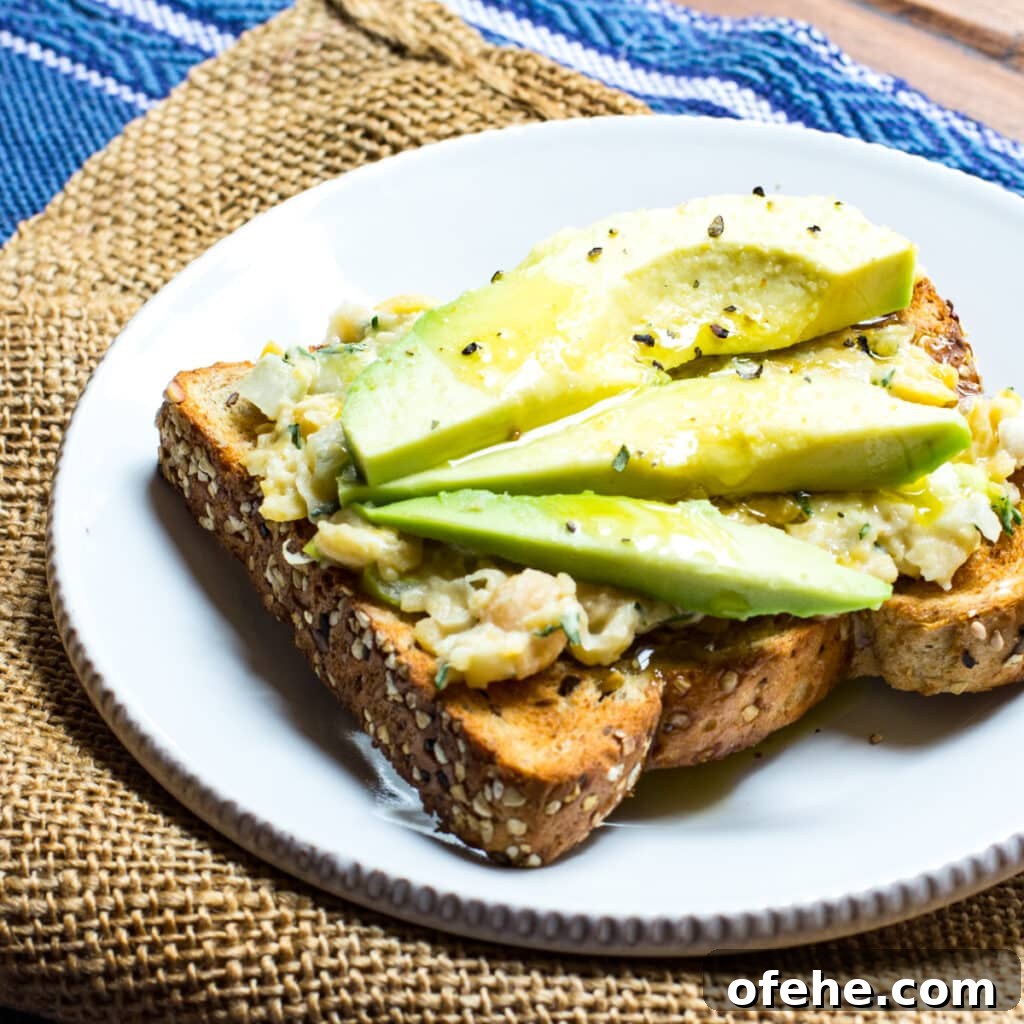 Chickpea salad spread on toast and topped with slices of avocado.