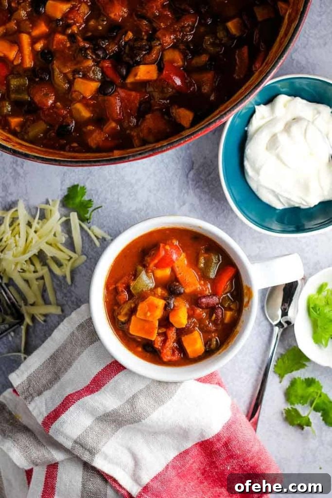 A bowl of vegetarian sweet potato chili with sour cream, grated cheese and cilantro on the side