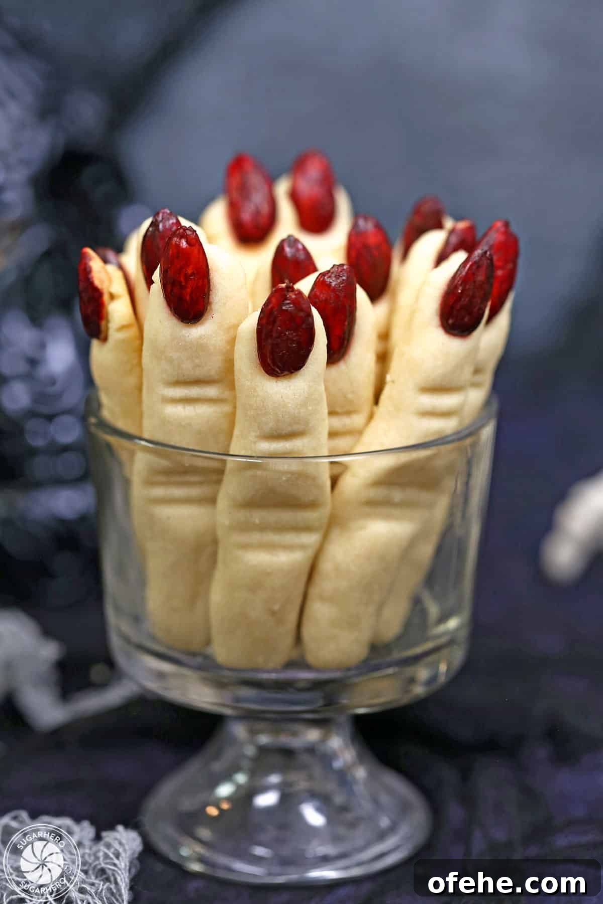 Spooky Witch Finger Cookie Recipe for Halloween Treats 2 Witch Finger Cookies upright in a glass, with a skull and silver pumpkin in the background.
