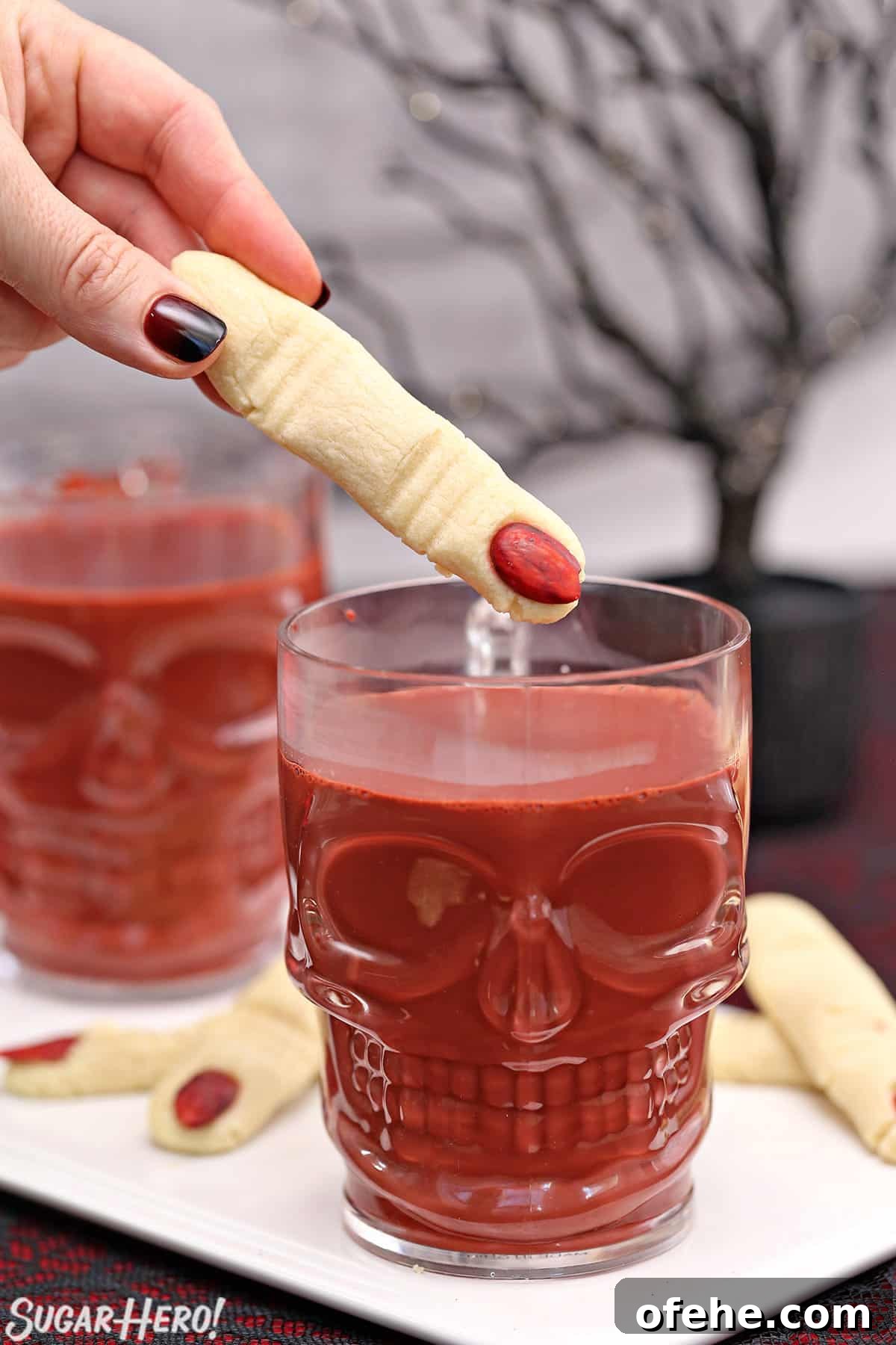 Spooky Witch Finger Cookie Recipe for Halloween Treats 22 Hand holding a finger-shaped cookie about to dunk it in a mug of red velvet hot chocolate.