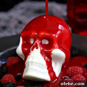 Spooky Witch Finger Cookie Recipe for Halloween Treats 10 Raspberry ganache being poured over white chocolate skull on a black plate with raspberries.