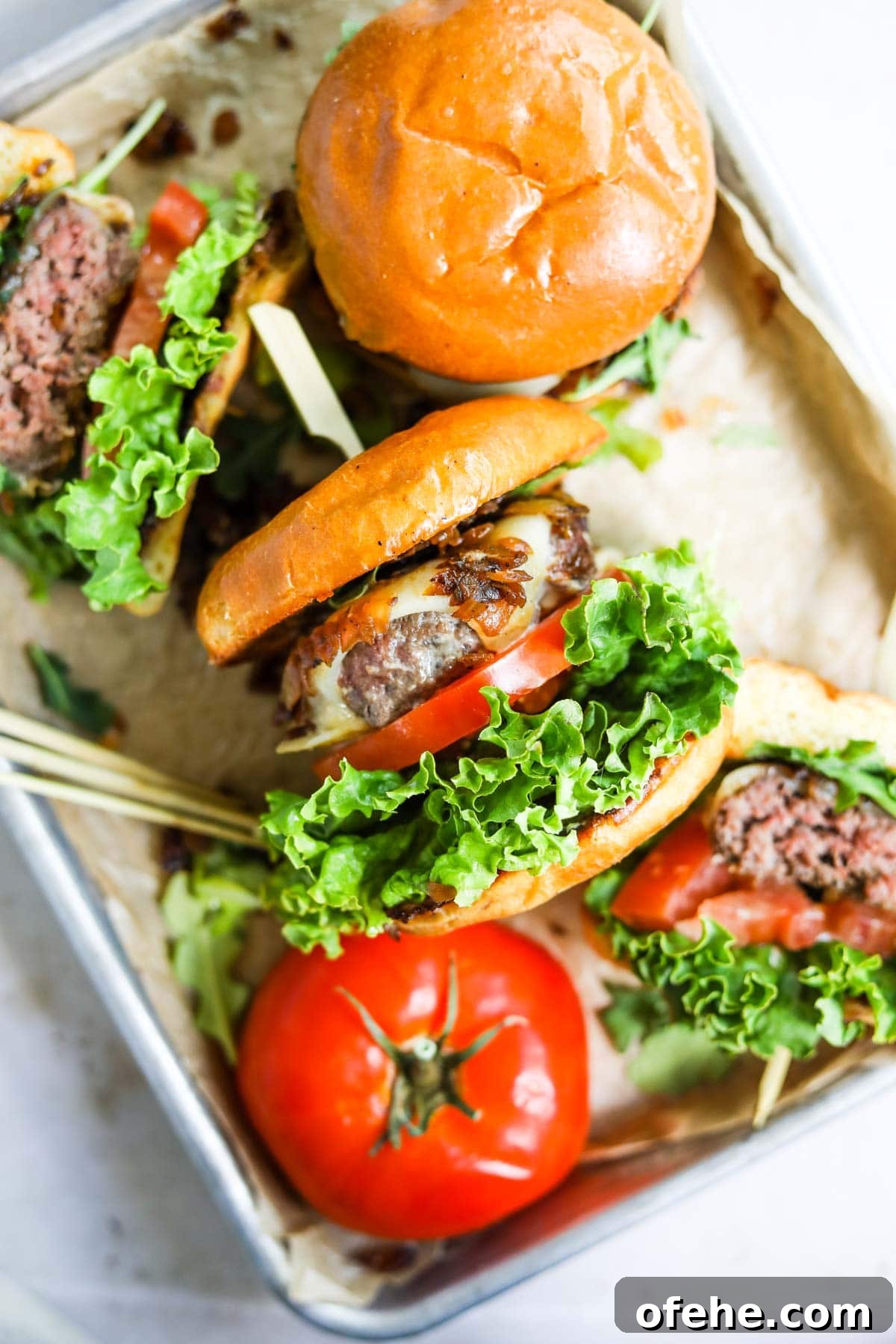 20 Delicious Dishes to Pair with Asparagus 10 Cast iron skillet burger made on a stovetop in a baking sheet with other burgers and sliced tomato.
