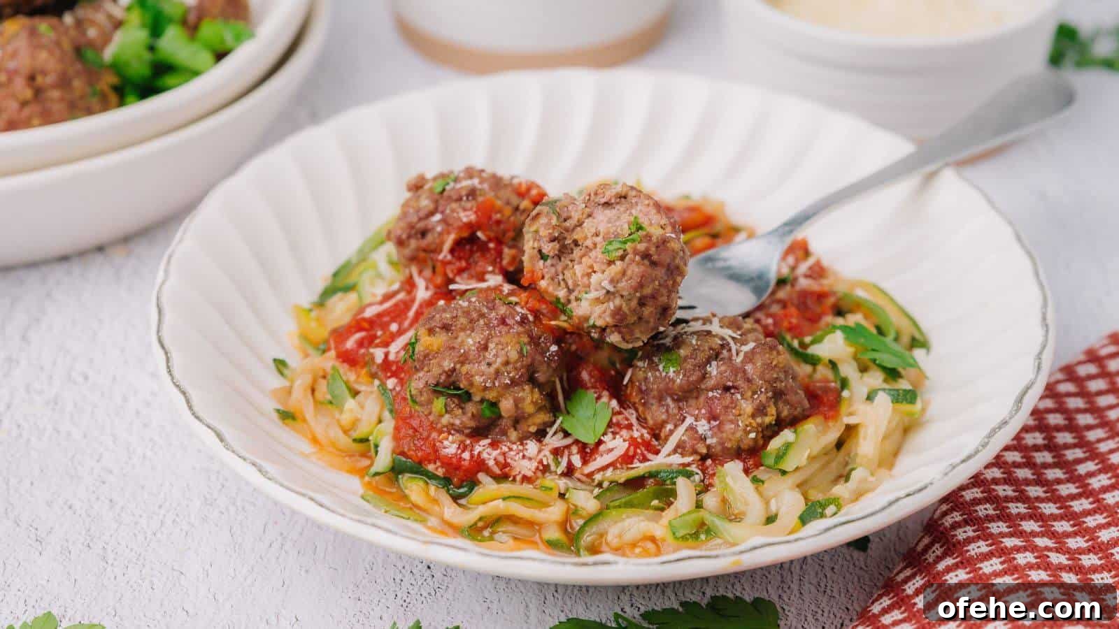 30 Quick Appetizers to Impress Guests Without Fuss 12 A plate of zucchini noodles topped with tomato sauce, meatballs, and grated cheese, garnished with parsley. A fork rests on the plate.