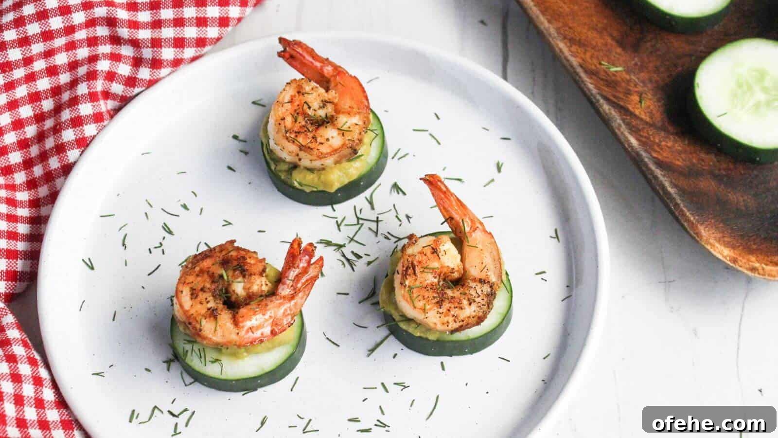 30 Quick Appetizers to Impress Guests Without Fuss 19 Three grilled shrimp atop cucumber slices garnished with herbs on a white plate with a red checkered napkin partially in view.