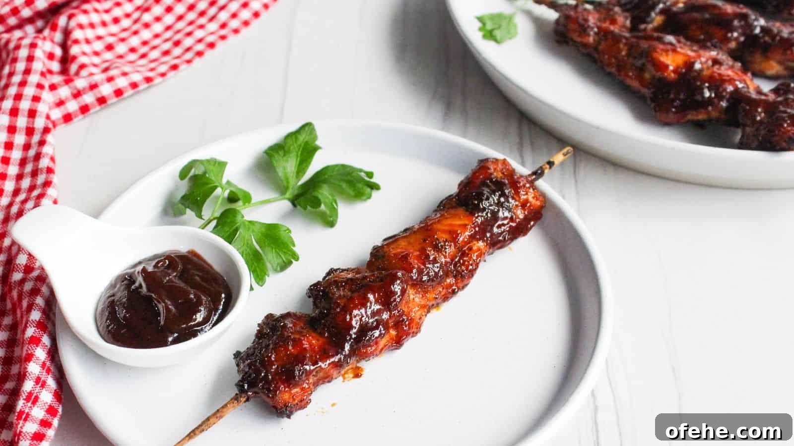 30 Quick Appetizers to Impress Guests Without Fuss 30 A single barbecued chicken skewer on a white plate, with a small bowl of barbecue sauce and a parsley garnish, next to a plate of additional chicken skewers.