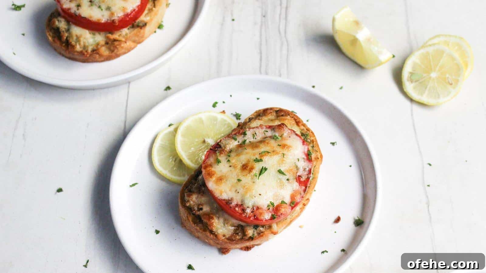 30 Quick Appetizers to Impress Guests Without Fuss 4 Two plates of crab melt with sliced tomatoes and melted cheese, garnished with lemon slices on a white wooden surface.