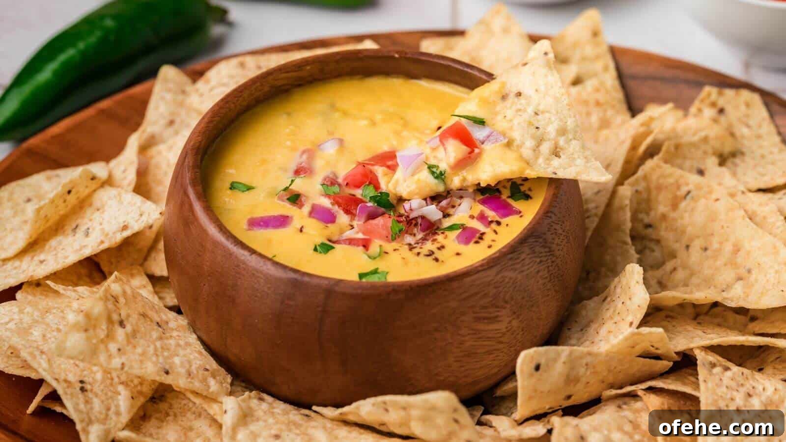 30 Quick Appetizers to Impress Guests Without Fuss 8 A wooden bowl of cheese dip topped with diced tomatoes and onions, surrounded by tortilla chips on a wooden platter.