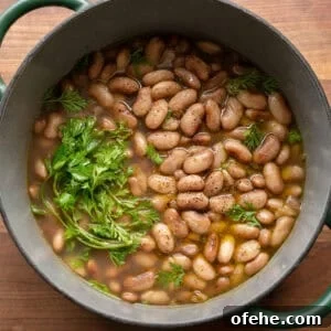 How to Perfectly Cook Dried Beans: Step-by-Step Guide 18 pot of brothy beans in a green saucepan on a wooden cutting board.