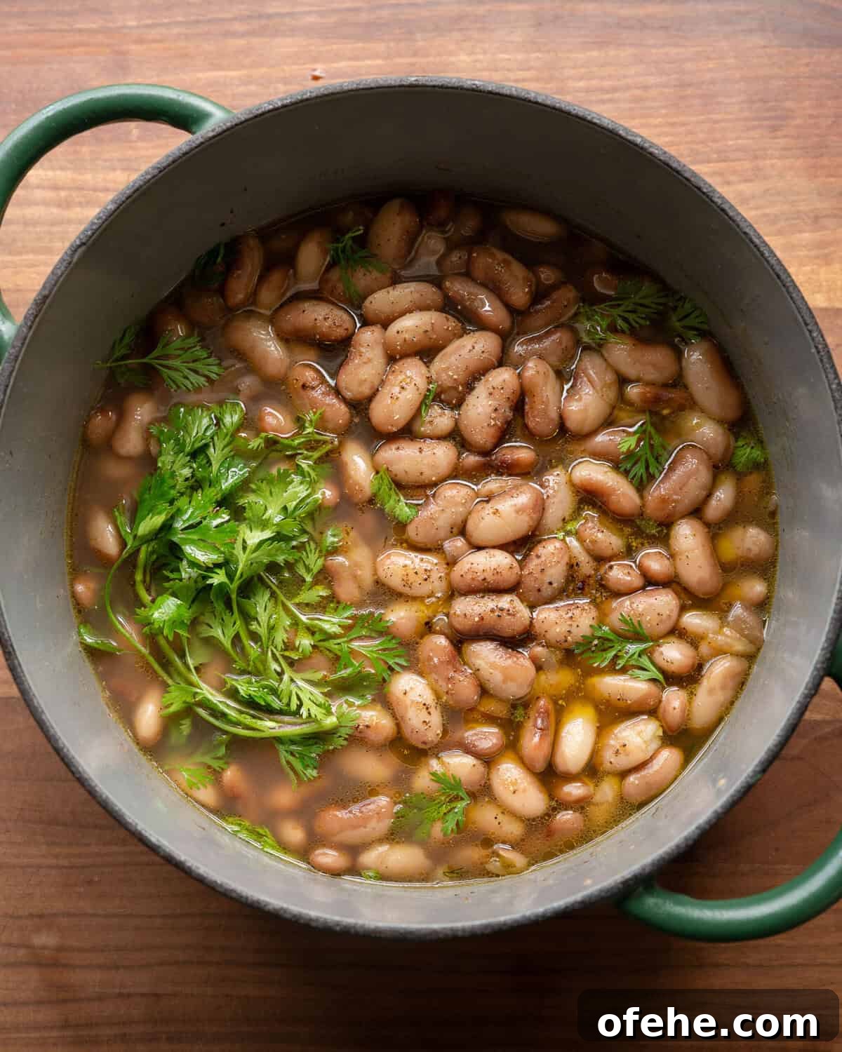 How to Perfectly Cook Dried Beans: Step-by-Step Guide 2 pot of brothy beans in a green saucepan on a wooden cutting board.