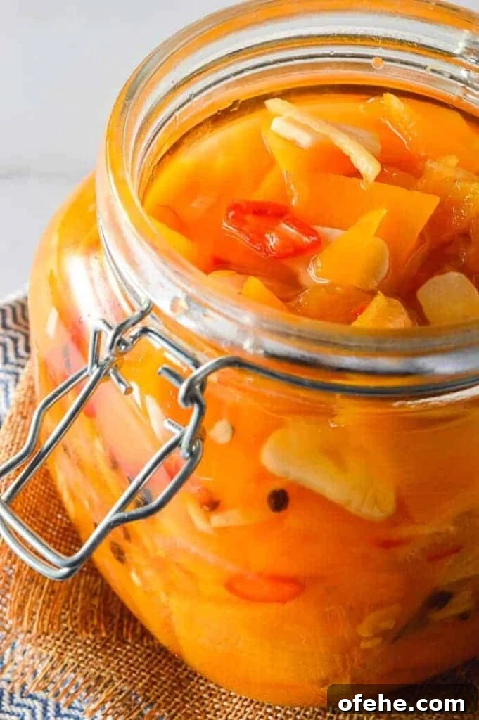 View into a glass jar with clear liquid, orange vegetable slices, garlic and red chilis