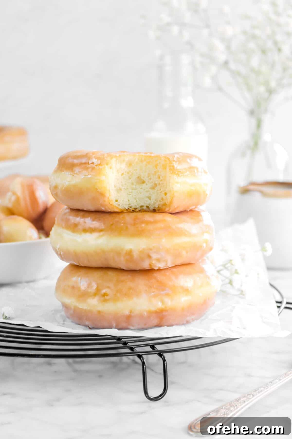 three stacked doughnuts on wire cooling rack with parchment, a bite taken out of doughnut, and more doughnuts behind