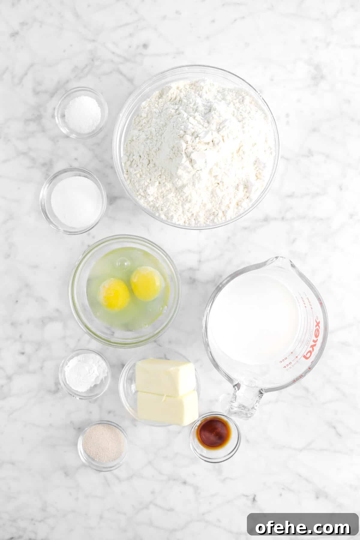 salt, sugar, flour, eggs, milk, butter, baking powder, yeast, and vanilla on marble counter