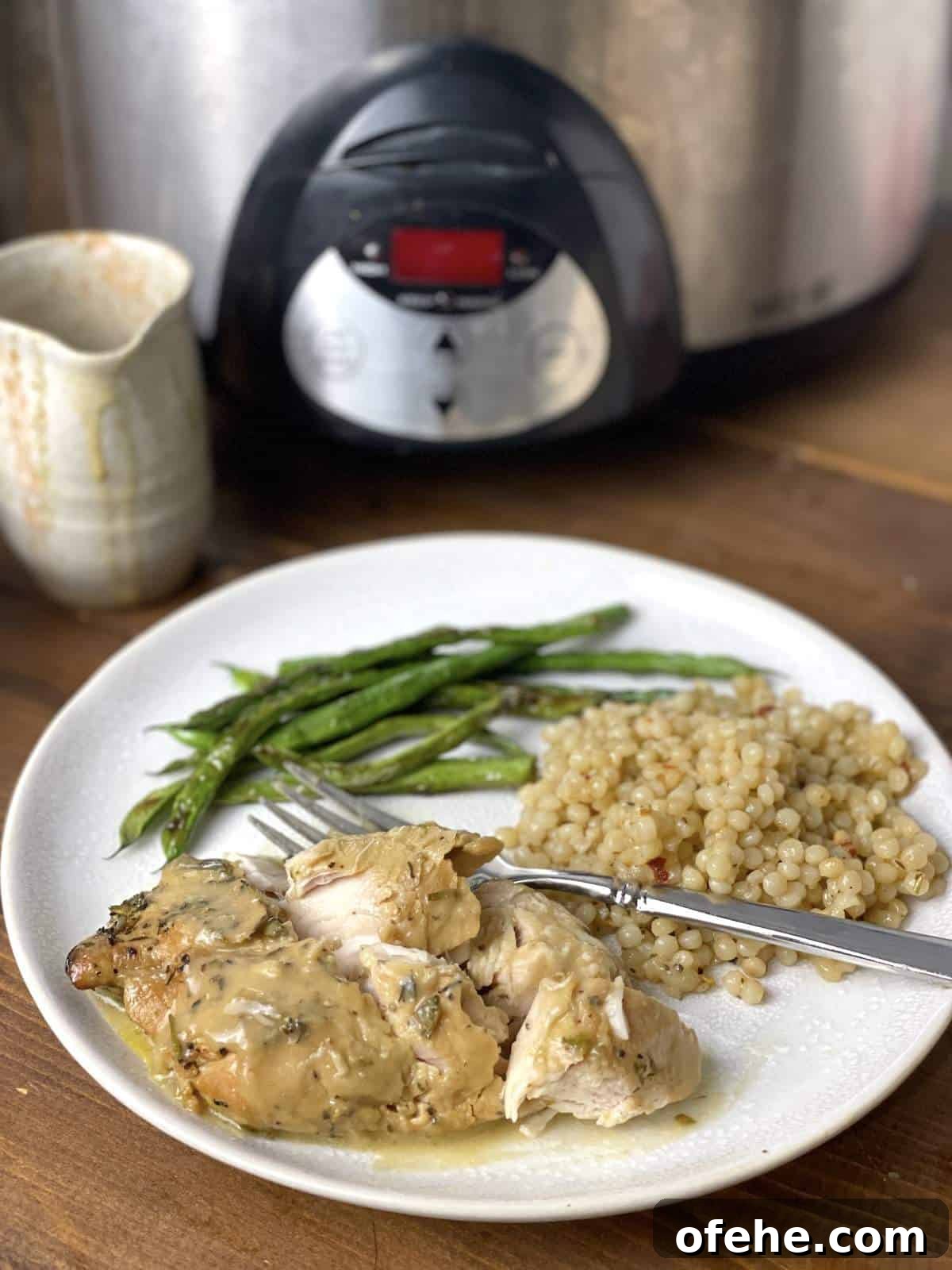 Crockpot Turkey Tenderloins in Honey Mustard Gravy 2 A cut up honey mustard turkey tenderloin with Israeli couscous and green beans on a plate with a fork in front of a crockpot.