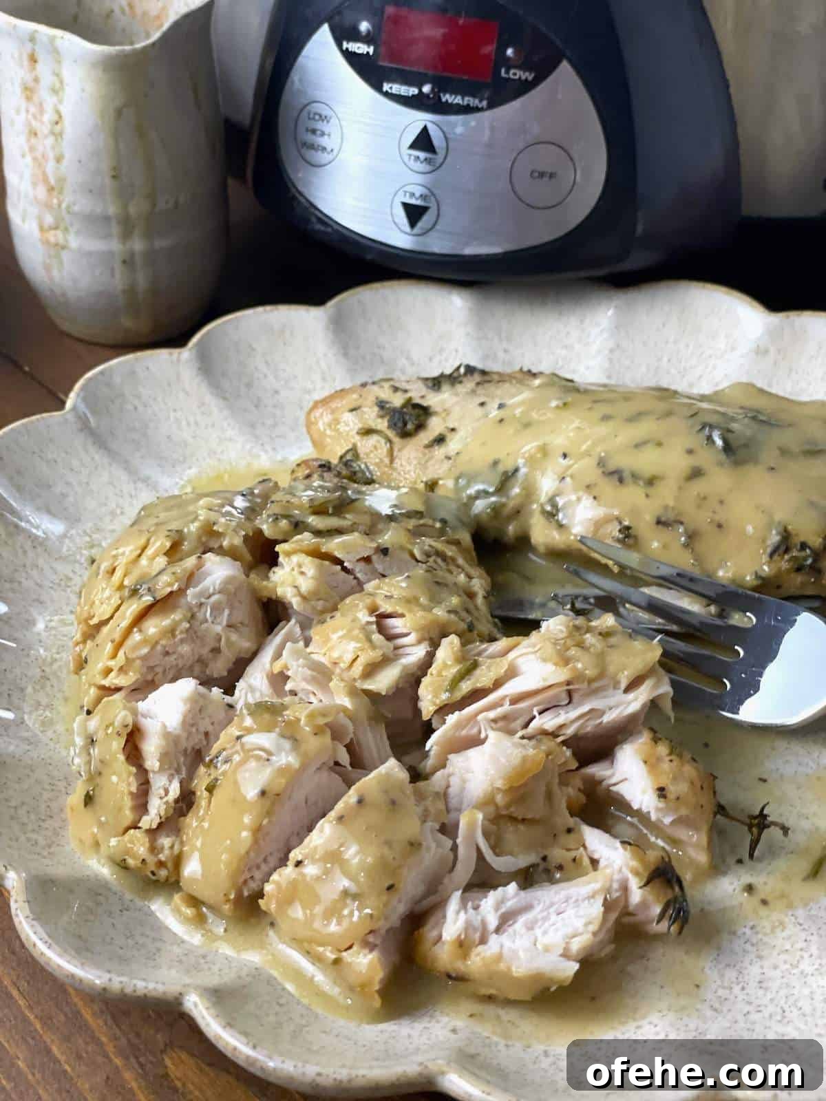 Crockpot Turkey Tenderloins in Honey Mustard Gravy 7 A cut up turkey tenderloin covered in gravy on a scalloped plate in from of a crockpot.