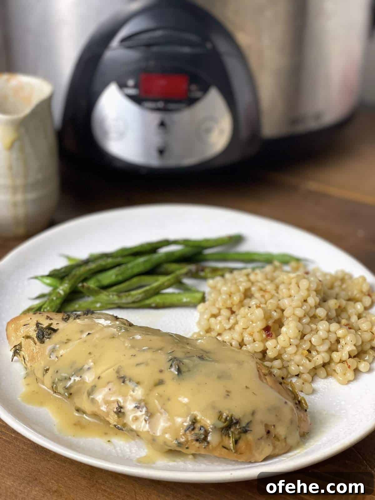 Crockpot Turkey Tenderloins in Honey Mustard Gravy 9 A cooked turkey tenderloin with Israeli couscous and green beans on a plate in front of a crockpot.