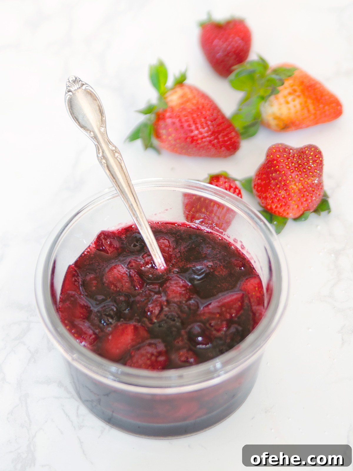 Fruit Compote Ideas: Delicious Pancake Toppers and More 2 Fruit compote in a clear bowl with a silver spoon and strawberries in the background.