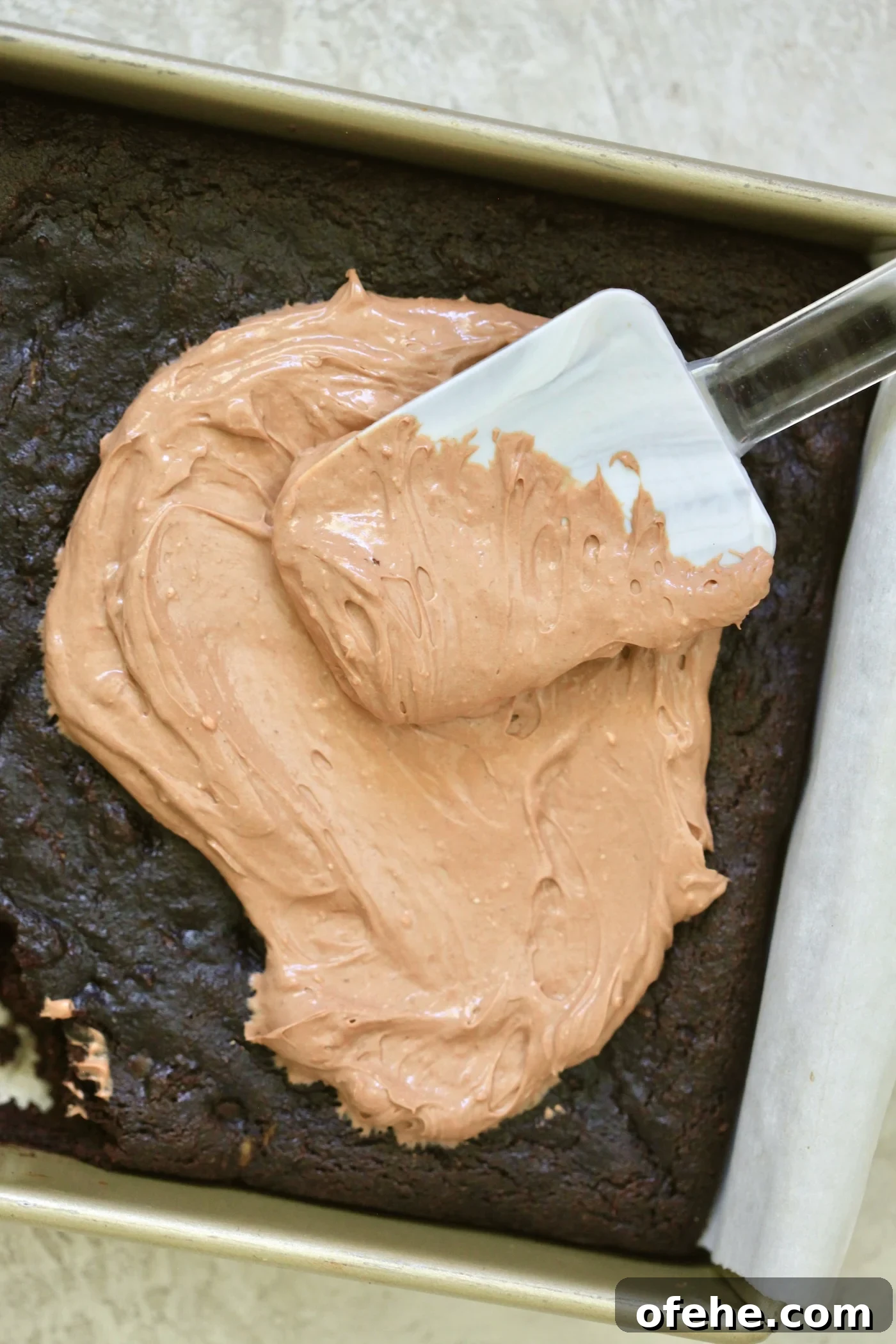 Decadent Chocolate Zucchini Cake That Actually Nourishes 9 spreading chocolate frosting with spatula on cake.