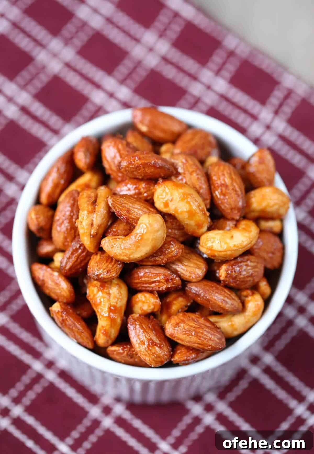 Maple Sriracha Roasted Nuts Recipe — Sweet-Spicy Snack Guide 2 maple sriracha roasted nuts in a white dish on a burgundy tea towel.