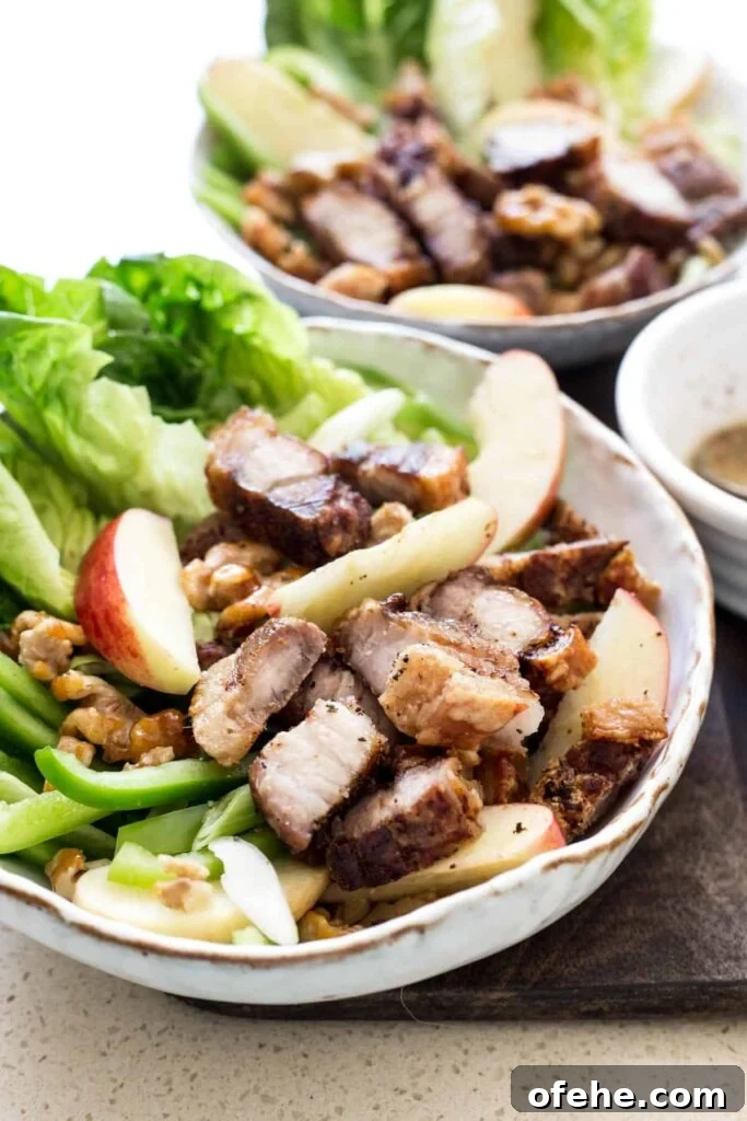 Roast Pork Belly Apple & Caramelised Walnut Salad in a white bowl on a wooden board