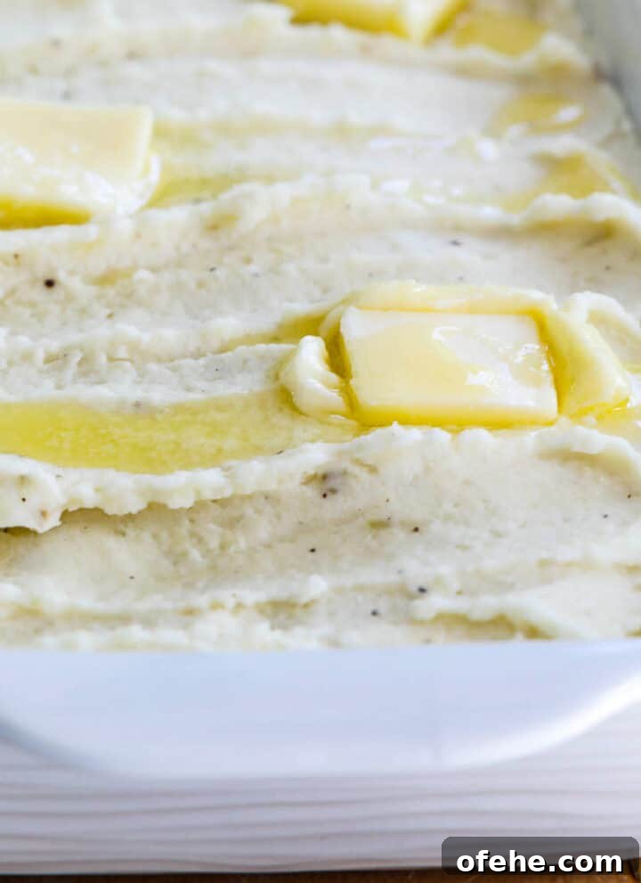 A white casserole dish filled with mashed potatoes and squares of melted butter on top.
