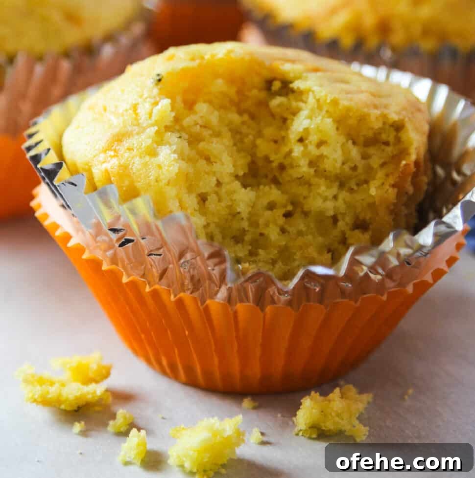 Cheddar Jalapeño Cornbread Recipe with Sweet Corn 15 A cornbread muffin in an orange muffin tin paper with a piece out of it and crumbs on the table.