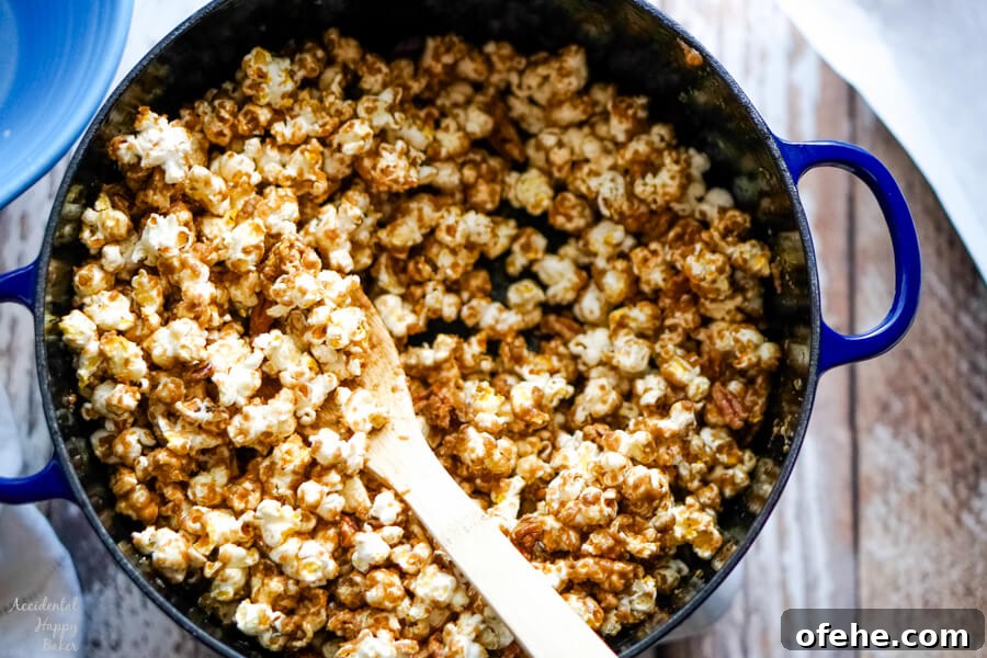 Salted Caramel Pecan Popcorn Recipe — Sweet & Crunchy Snack 7 A blue dutch oven of caramel corn with a wooden spoon.