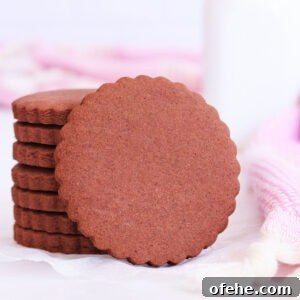 A stack of scalloped-edge round gluten free chocolate cookies, with one cookie resting on its side against the stack.