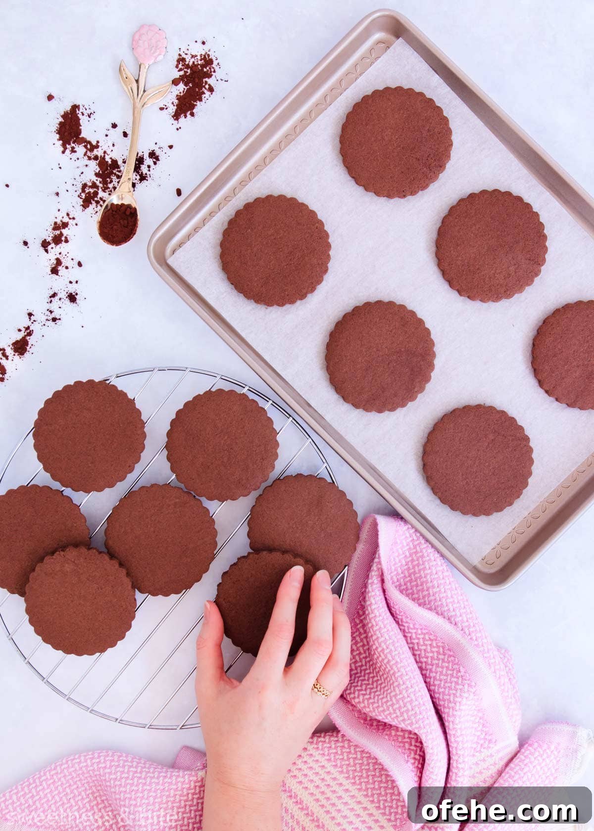 Cookies on a baking tray and arranged on a round cooling rack, with a hand taking a cookie.