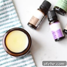 DIY Natural Vapor Rub with Essential Oils for Congestion Relief 4 an amber glass jar with homemade vapor rub in it with a striped green and white towel laid under it and essential oils laying next to it