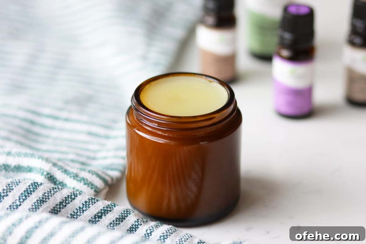 DIY Natural Vapor Rub with Essential Oils for Congestion Relief 6 an amber glass jar with homemade vapor rub in it with a striped green and white towel laid under it and essential oils laying next to it