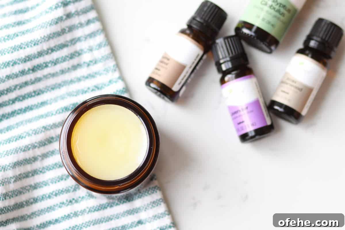 DIY Natural Vapor Rub with Essential Oils for Congestion Relief 7 an amber glass jar with homemade vapor rub in it with a striped green and white towel laid under it and essential oils laying next to it
