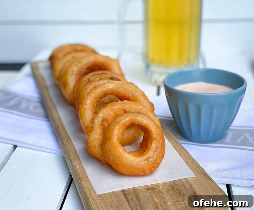onion rings on a wooden plank with a beer and sauce next to them.