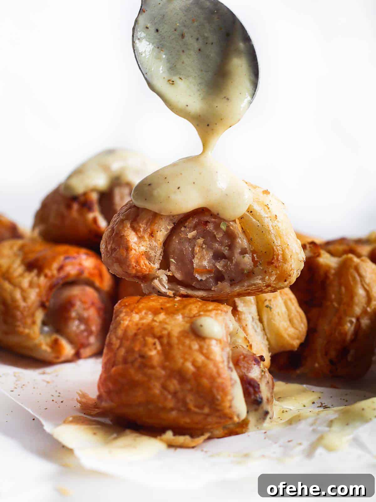 Puff pastry pigs in a blanket with sauce spooned over top.