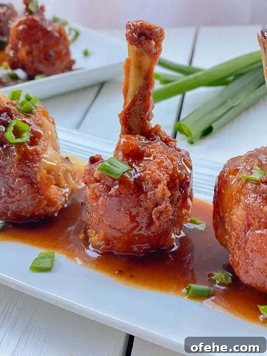 lollipop chicken wings standing upright on a white plate smothered in sauce.
