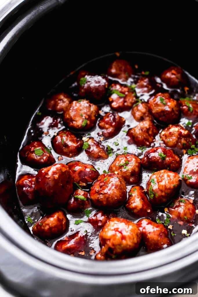football meatballs in a crock pot sitting in a sweet spicy sauce.
