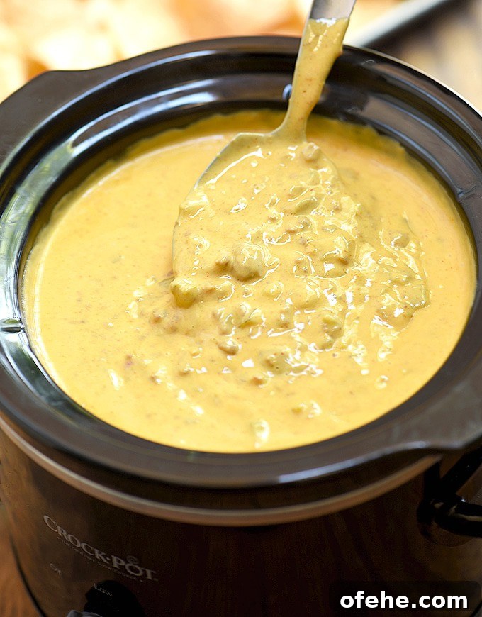 melted queso cheese with beer inside of a slow cooker with a spoon.