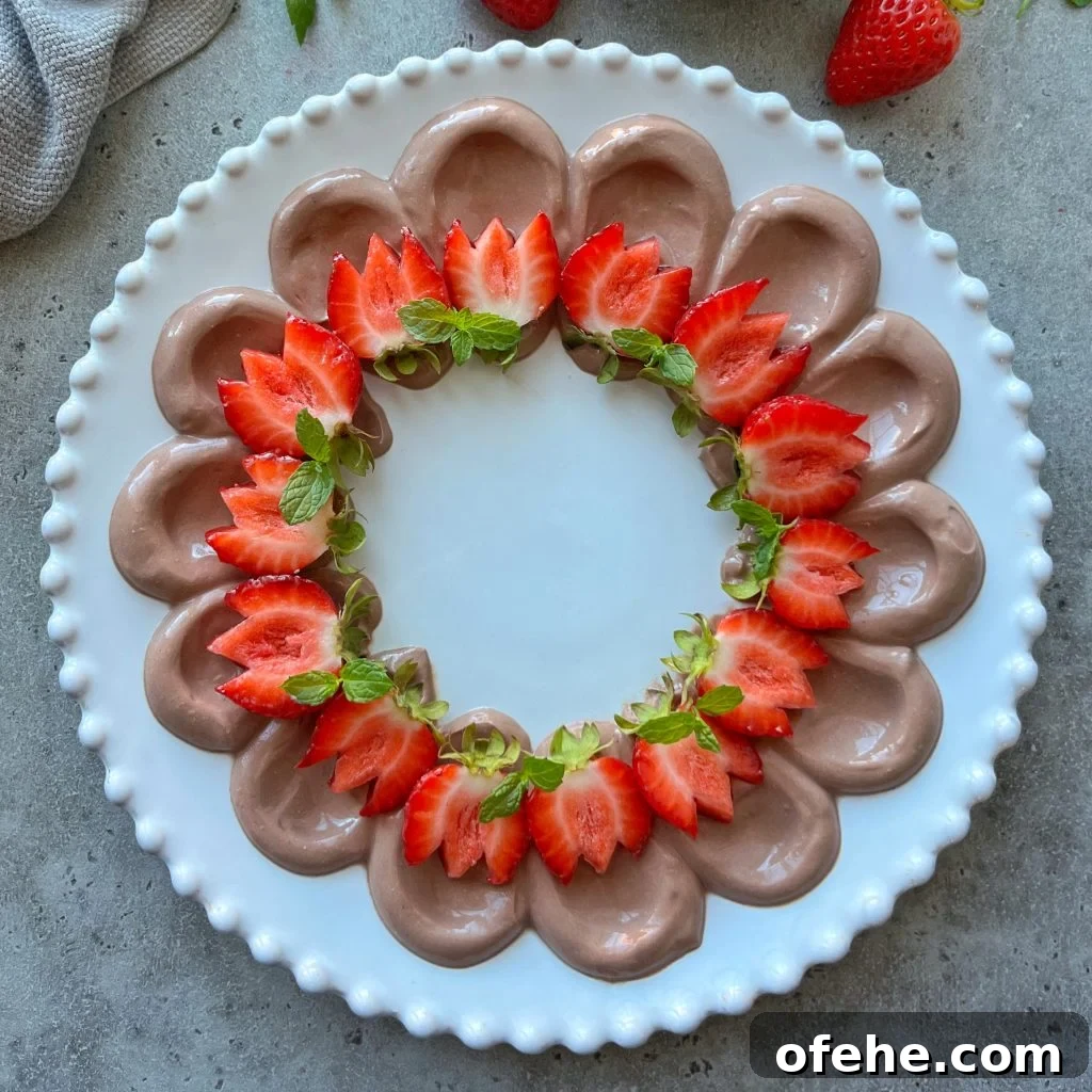 Creamy Fruit Yogurt Dip Recipe for Parties and Snacks 2 A round white plate with dollops of chocolate dip piped in a circle, topped with halved strawberries and fresh mint leaves, forming a decorative ring on a gray surface.