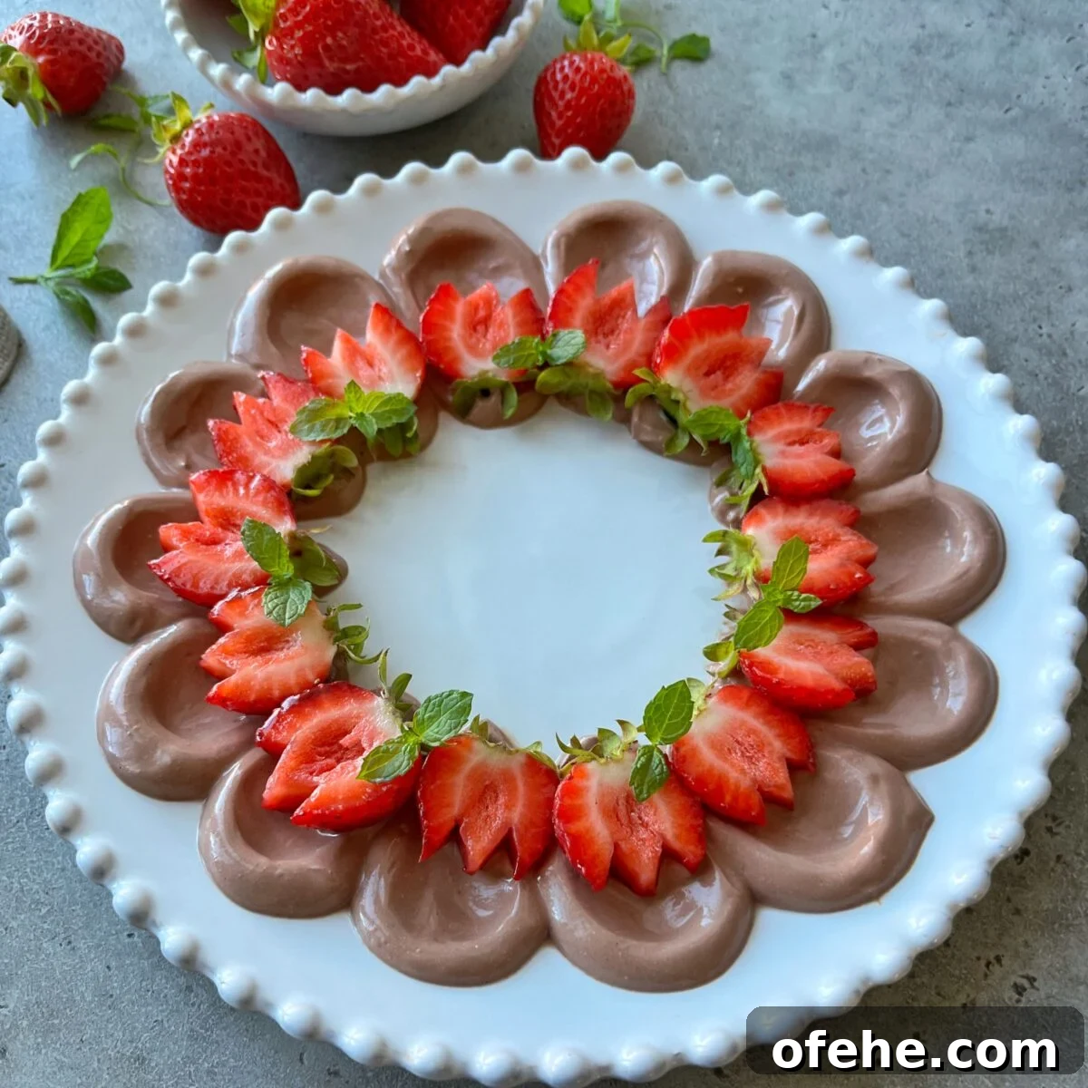 Creamy Fruit Yogurt Dip Recipe for Parties and Snacks 3 A white plate with chocolate dip piped in a ring, topped with sliced strawberries arranged in a circular pattern. A bowl of strawberries sit in the background.