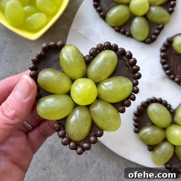 Creamy Fruit Yogurt Dip Recipe for Parties and Snacks 6 A hand holds a Grape Chocolate Heart—a heart-shaped chocolate base decorated with green grapes arranged like flower petals.
