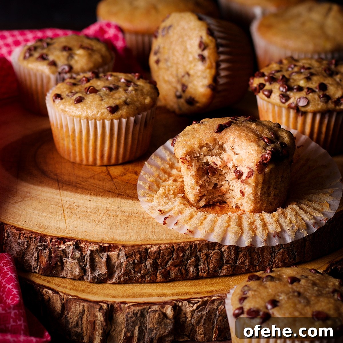 A gluten free chocolate chip banana muffin with a bite taken out of it on a wood serving platter.