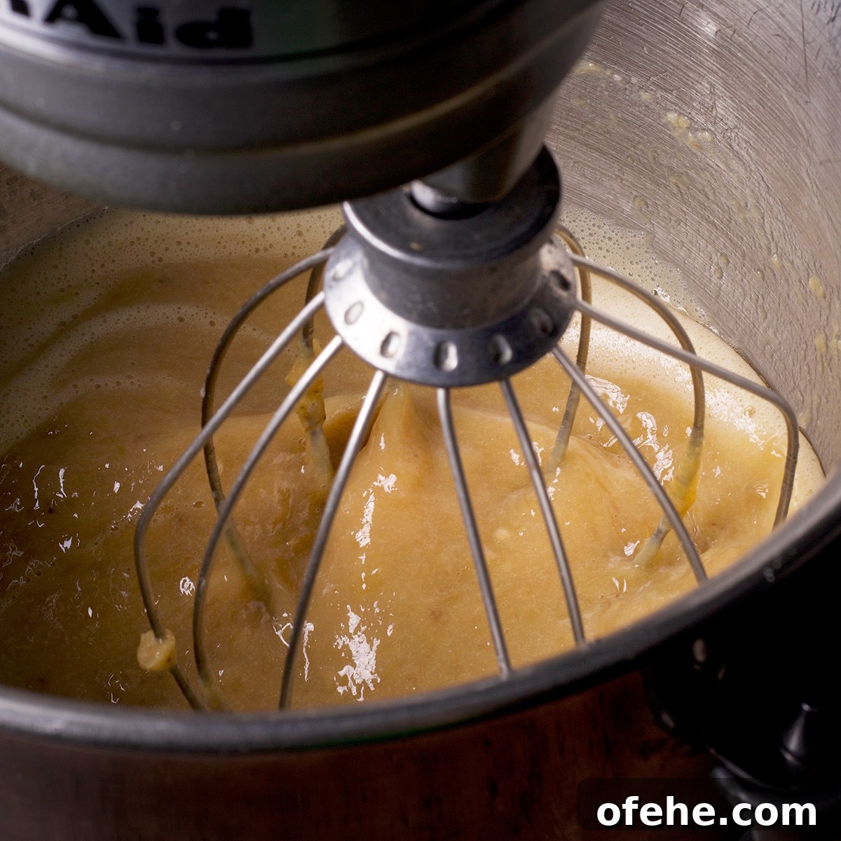 Looking down into the bowl of a stand mixer while it beats the wet ingredients for gluten free banana muffin batter.