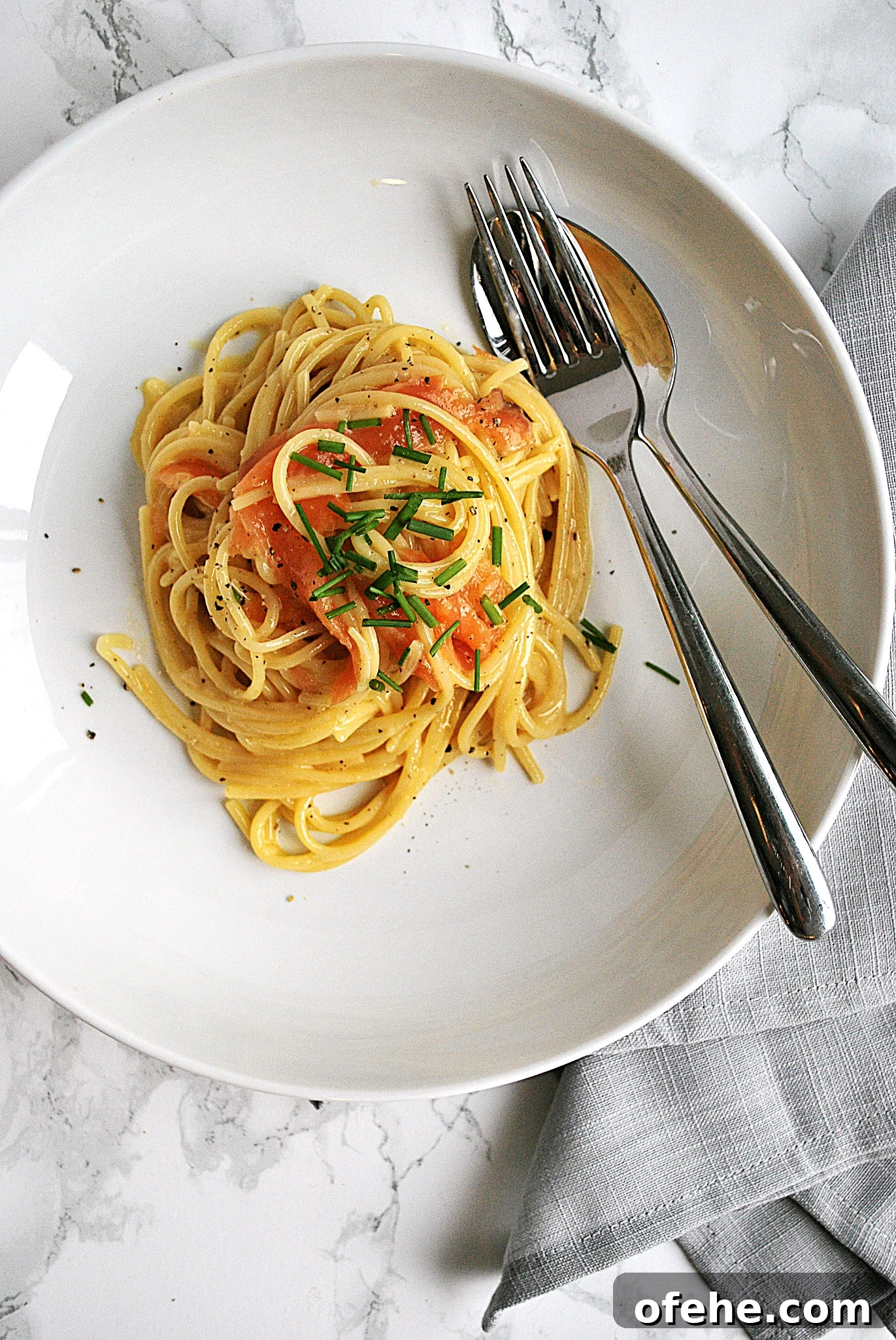 A plate with creamy smoked salmon spaghetti carbonara beside a napkin and cutlery.