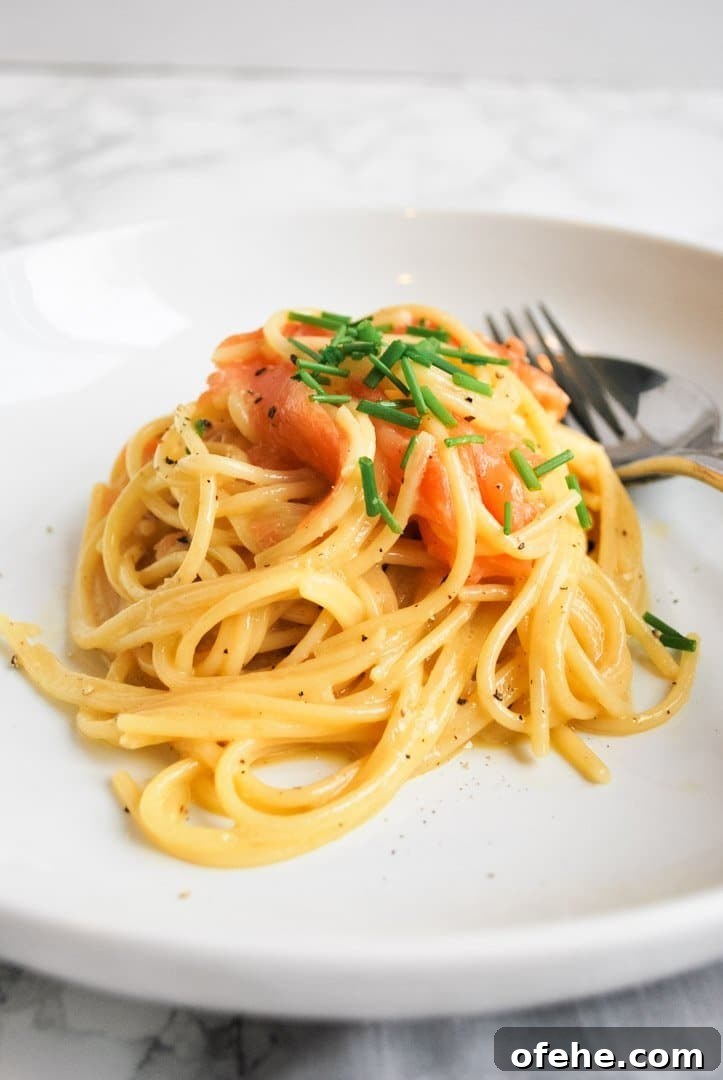 A white plate with a portion of smoked salmon carbonara in the middle of it.