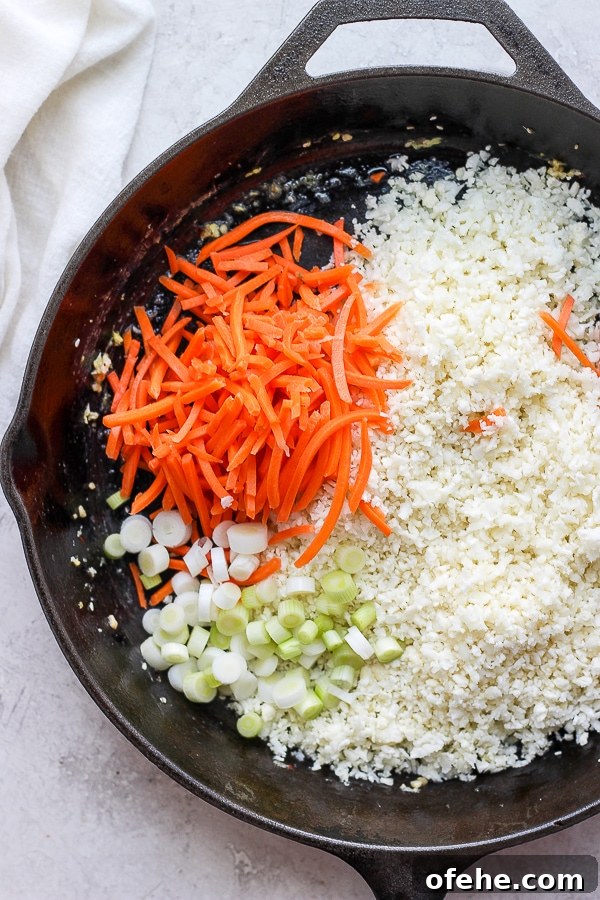 Shrimp Fried Cauliflower Rice - for when you are craving take-out, but also want to eat clean! (Paleo + Whole30 + Gluten-Free) #whole30recipes #shrimpfriedcauliflowerrice #paleorecipes #easyweeknightdinners Cauliflower rice, onion and carrots in a cast iron skillet.