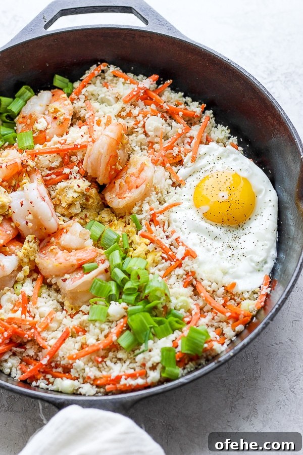 Shrimp Fried Cauliflower Rice - for when you are craving take-out, but also want to eat clean! (Paleo + Whole30 + Gluten-Free) #whole30recipes #shrimpfriedcauliflowerrice #paleorecipes #easyweeknightdinners Shrimp fried cauliflower rice in a cast iron skillet with fried egg on top.